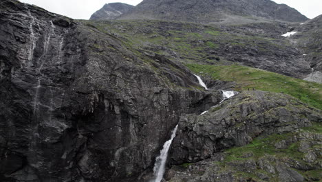 Toma-Aérea,-Saliendo-De-Una-Cascada-Que-Se-Precipita-Sobre-Una-Pared-Rocosa-Escarpada,-Cerca-De-Trollstigen,-Noruega