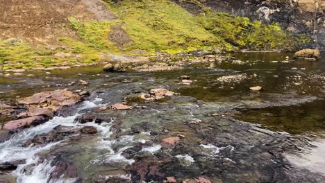 Gentle-river-flowing-in-front-of-Glymur,-Iceland's-second-highest-waterfall,-surrounded-by-green-mossy-cliffs