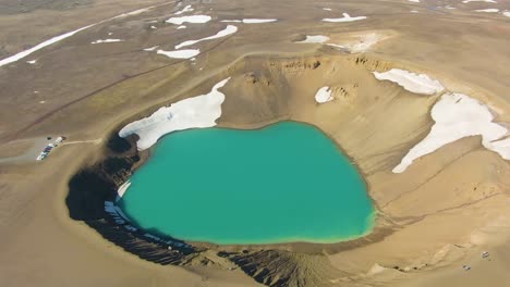 Eine-4K-Drohne-Hat-Filmreife-Luftaufnahmen-Eines-Smaragdgrünen-Sees-Inmitten-Einer-Landschaft-Gemacht,-In-Der-Schmelzender-Schnee-Die-Szenerie-Dominiert