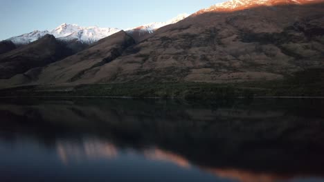 Luftaufnahmen-Fliegen-In-Richtung-Der-Perfekt-Reflektierten-Schneebedeckten-Berge-Bei-Sonnenuntergang-In-Der-Nähe-Von-Queenstown,-Neuseeland