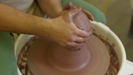 Creative-potter-forming-handmade-wet-clay-vase-vessel-spinning-on-workshop-pottery-wheel