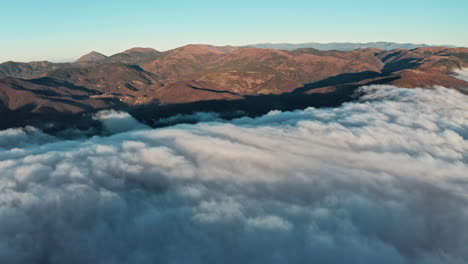 Mountain-peaks-emerging-above-sea-of-clouds-during-sunrise,-aerial-shot