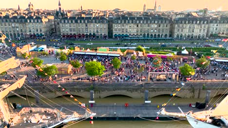 Wood-sailing-ships-in-the-Garonne-River-during-Wine-Fair-with-large-crowds-near-shore,-Aerial-pan-right-shot