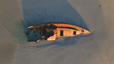 A-rising-top-down-shot-of-a-wrecked-boat-in-sand-on-a-beach-at-Carpenter-Rocks,-South-Australia