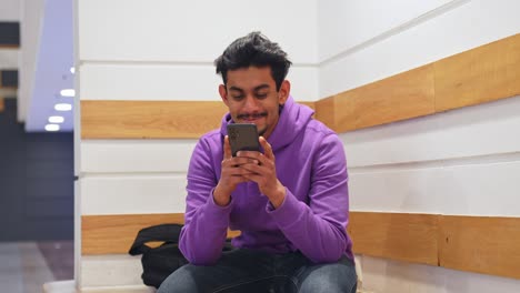 Glücklicher-Sri-lankischer-Mann-Mit-Lila-Pullover-Schaut-Auf-Sein-Smartphone