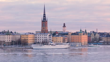 Iconic-Riddarholmen-Church-in-Gamla-Stan,-aerial-pullback-over-icy-Riddarfjarden