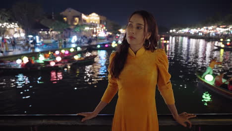 Joven-Vietnamita-Posando-Con-Un-Tradicional-Vestido-Amarillo-En-La-Escena-Del-Río-Nocturno-En-Hoi-An,-Vietnam