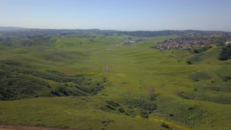 An-aerial-view-of-a-large-vacant-ranch-in-a-lush-green-valley-surrounded-by-housing-development