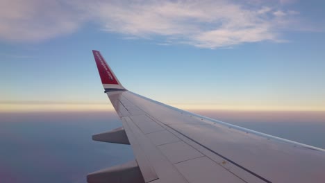 POV-from-window-by-wing-of-Norwegian-airplane-high-in-blue-cloudy-sky