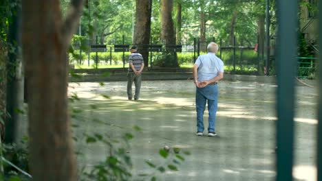 Peeking-Shot-of-Elderly-Italian-Men-Playing-Bocce-Ball-Bowls-in-Green-Park
