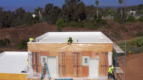 Toma-Aérea-Descendente-De-Primer-Plano-De-Un-Equipo-De-Construcción-Trabajando-En-El-Revestimiento-De-Un-Módulo-De-Vivienda-Prefabricado-En-Un-Sitio-De-Construcción-En-El-Oeste-De-Los-Ángeles,-California.