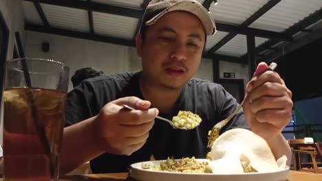 An-Indonesian-man-eats-fried-rice-or-Nasi-Goreng-with-a-spoon-and-fork-in-a-cafe_slow-motion