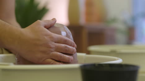 Male-craftsman-hands-wet-raw-clay-material-on-studio-pottery-wheel-close-up-shot