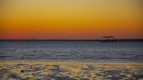 Hermoso-Amanecer-En-El-Horizonte-En-La-Playa-Con-Un-Muelle-En-El-Mar-Y-Pequeñas-Islas-Al-Fondo