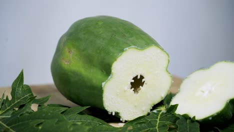 Schöne-Aufnahme-Einer-Aufgeschnittenen-Grünen-Papaya-Auf-Einem-Tisch-Und-Grünen-Blättern-Rundherum