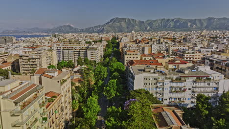 Palermo-Italy-Aerial-v9-drone-fly-along-Via-della-Liberta-capturing-tree-lined-street,-historic-buildings,-city-urban-park-and-mountain-landscape-on-the-skyline---Shot-with-Mavic-3-Cine---May-2023