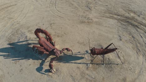 Aerial-shot-looking-straight-down-at-a-scorpion-and-a-grasshopper-statue,-the-revealing-a-stunning-blue-mountainous-landscape-in-the-background