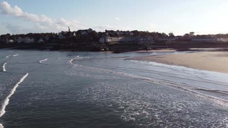 Drones-Vuelan-Sobre-El-Agua-Del-Océano-Con-El-Paisaje-Urbano-De-Ogunquit-A-Distancia-Durante-La-Puesta-De-Sol,-Antena-De-La-Costa-En-Maine-Usa