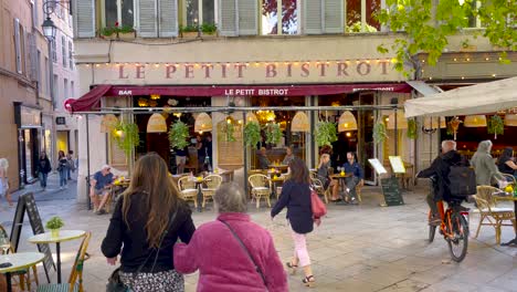 People-move-by-French-restaurant-on-square-in-Aix-en-Provence,-France