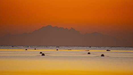 Hermosos-Lapsos-De-Tiempo-Del-Mar-Con-Un-Cielo-Colorido-Al-Atardecer,-Al-Fondo-La-Silueta-De-Una-Montaña