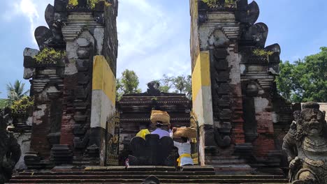 Bali-Women-With-Baskets-on-Head-Going-Through-Gate-of-Ancient-Hindu-Temple,-Ubud