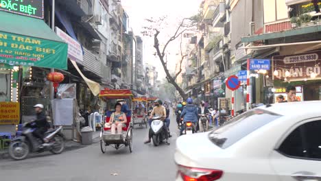 Bustling-Hanoi-street-with-cyclists-and-motorbikes,-vibrant-storefronts,-and-local-charm,-daytime