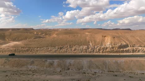 Car-zooming-by-heading-north-on-a-Desert-highway-with-cloudy-blue-sky