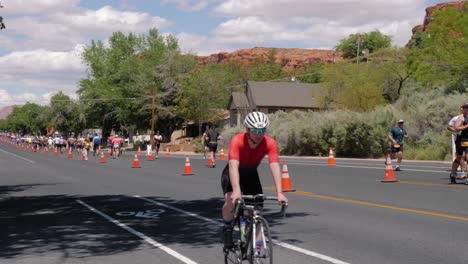 Toma-En-Cámara-Lenta-De-Un-Ciclista-Con-Camisa-Roja-Y-Corredores-En-El-Ironman-70-De-Salud-Entre-Montañas