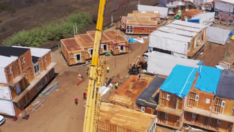 Aerial-descending-and-tilting-up-shot-of-a-heavy-duty-lift-crane-at-a-modular-housing-construction-site-in-West-Los-Angeles,-California