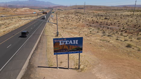 Welcome-to-Utah-USA,-drone-aerial-view-of-state-road-sign-on-Nevada-border-and-traffic-on-highway-on-hot-sunny-day