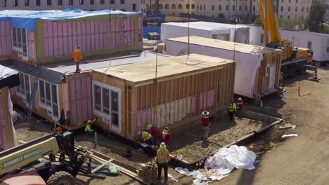 Aerial-reverse-pullback-close-up-shot-of-a-heavy-duty-lift-crane-lowering-a-pre-fabricated-housing-module-into-position-at-a-building-site-in-West-Los-Angeles,-California