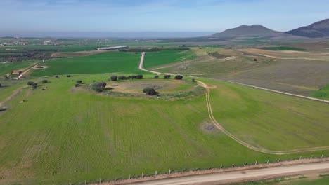 Vuelo-Viendo-Los-Restos-De-Un-Gran-Dolmen-Y-El-Paso-De-Una-Bandada-De-Pájaros-Blancos-En-Un-Entorno-De-Verdes-Campos-De-Cultivo-Con-Un-Fondo-De-Montañas-Con-Un-Cielo-Azul-En-Invierno-Toledo,-España