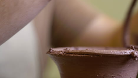 Artisan-craftsman-trimming-wet-clay-vessel-neck-close-up-on-workshop-pottery-wheel