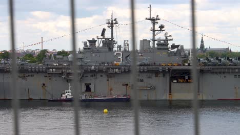 Huge-US-navy-ship-USS-Kearsarge-in-still-water-seen-through-metal-bars