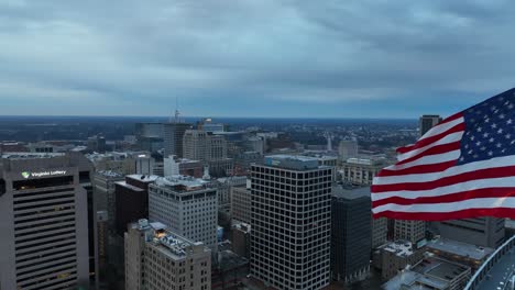 Primer-Plano-Aéreo-De-Una-Bandera-Americana-Ondeando-Sobre-El-Horizonte-De-La-Ciudad