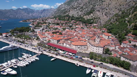 Kotor-Old-Town,-Montenegro,-Aerial-View-of-Medieval-Fort,-Traffic-by-Harbor-and-Bay-on-Sunny-Day,-Drone-Shot