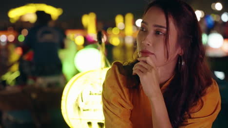 Woman-in-Ao-Dai-pondering-at-night-in-vibrant-Hoi-An,-colorful-lanterns-in-background,-close-up