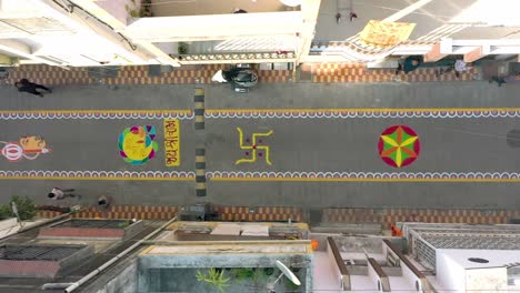 aerial-drone-view-camera-many-people-are-looking-at-the-drone-camera-and-many-people-are-looking-at-big-sathiyo-and-big-big-rangoli-is-seen-between-them