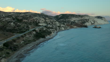 Abenddämmerung-Blick-Auf-Eine-Kurvenreiche-Straße,-Die-Durch-Eine-Hügelige-Landschaft-Führt-Zu-Einem-Küstenstrand-Mit-Weißen-Kreidefelsen,-Mit-Einem-Hintergrund-Von-Rosa-Gefärbten-Wolken-Am-Himmel,-Pafos,-Afrodite-Hügel