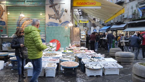 Pan-left-shot-of-street-market-in-Naples,-people-near-fish-stall,-Italy