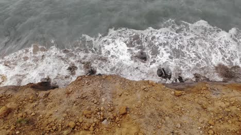 Aerial-overhead-shot-panning-right-looking-down-at-waves-crashing-against-a-huge-landslip-at-Seatown-Dorset-England