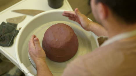 Over-shoulder-view-male-potter-working-raw-clay-material-on-studio-pottery-turntable-wheel