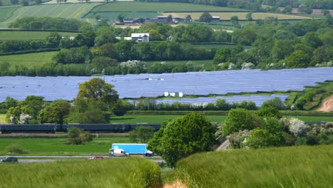 A-train-from-the-city-of-Exeter-and-motorway-traffic-on-the-M5-pass-between-a-barley-field-and-a-large-solar-farm-in-the-lush-Devon-countryside-near-Tiverton-Parkway-railway-station