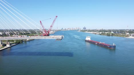 Cargo-vessel-passes-Gordie-Howe-international-bridge-being-built-over-Detroit-River,-connecting-the-US-and-Canada