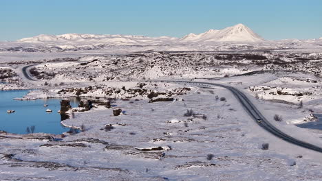 Car-drives-isolated-road-along-lake-in-snow-covered-landscape,-aerial