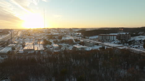 Wintery-sunrise-over-the-Dabrowa-district-in-Gdynia,-Poland,-casting-a-warm-glow-over-the-snow-covered-landscape-with-residential-buildings,-bare-trees,-and-a-prominent-radio-mast,-clear-afternoon-sky