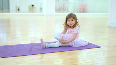 Hübsche-Kleine-Ballerina-In-Einem-Rosa-Tutu-Kleid-Streckt-Lächelnd-Die-Beine-Im-Leeren-Ballettstudio