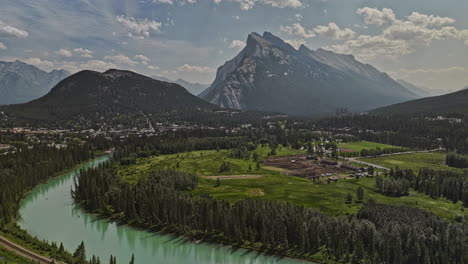 Banff-AB-Canada-Aerial-v47-picturesque-landscape-of-glacier-fed-Bow-river,-stables-in-meadows,-quaint-foothill-town,-forested-valley-and-Rundle-mountain-ranges---Shot-with-Mavic-3-Pro-Cine---July-2023