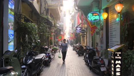 Vibrant-alley-in-Hanoi-with-walking-person,-neon-signs,-and-parked-scooters,-daytime