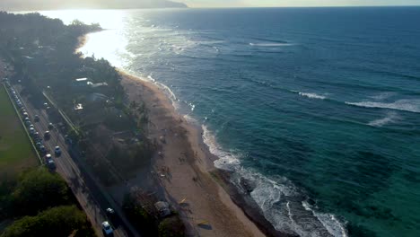 Sandy-beach-of-Hawaii-with-highway-nearby-on-sunny-day,-aerial-ascend-view